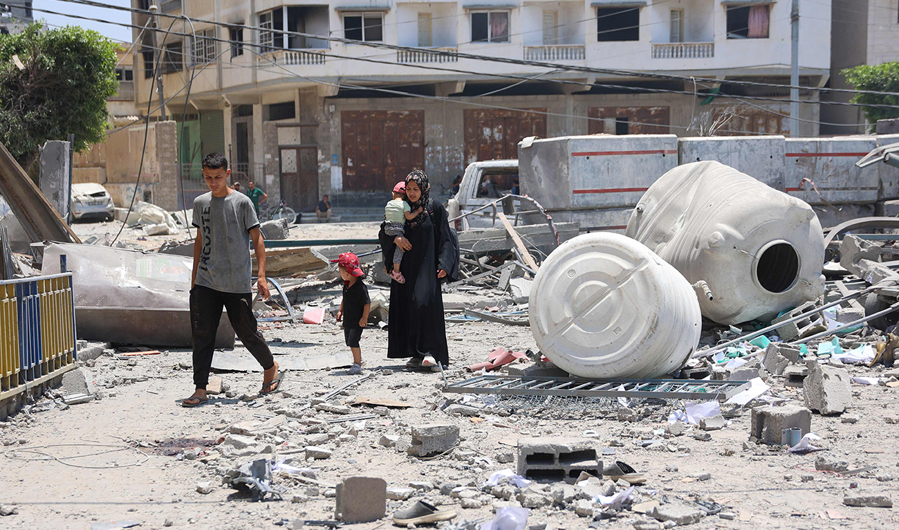 People walk next to rubble following Israeli bombardment on the security gate of the headquarters of the United Nations Relief and Works Agency for Palestine Refugees (UNRWA) in Gaza City on June 23, 2024, amid the ongoing battle between Israel and Hamas. (AFP)