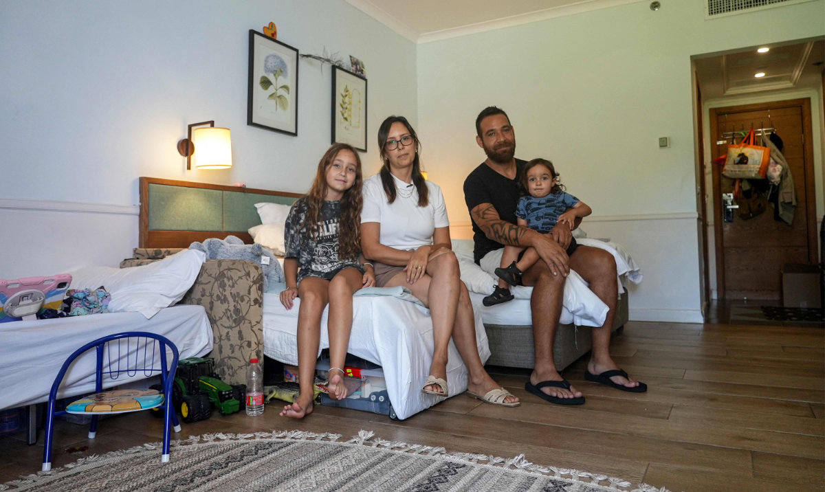 Yarden (C-L) and Edward (C-R) Gil sit with their two children to pose for a picture in a room at a hotel in Tiberias on June 21, 2024 where they have been living for over eight months after being displaced from their home in kibbutz Yiftah in northern Israel along the border with Lebanon. (AFP)