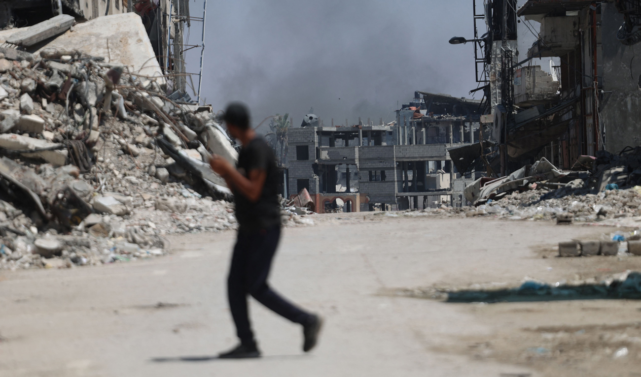 A Palestinian man crosses a street with smoke billowing in the background from an area targeted by Israeli bombardment in the Gaza City district of Shujaiya on June 28, 2024, amid the ongoing conflict between Israel and Hamas. (AFP)