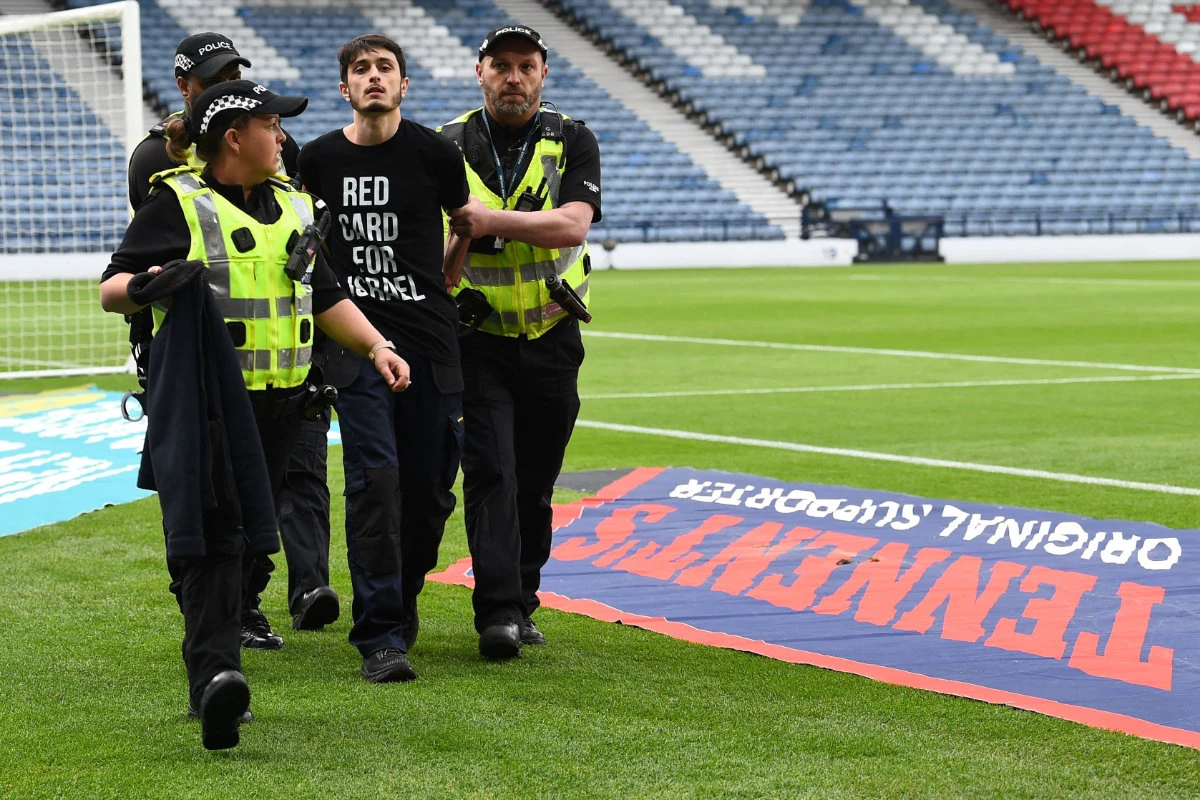 A demonstrator wearing a t-shirt reading "Red card for Israel" is escorted out by police officers from the Hampden Park stadium in Glasgow, Scotland, after he chained himself to the goal post prior to the UEFA Women's Euro 2025 League B Group 2 qualifying football match on May 31, 2024. (AFP)