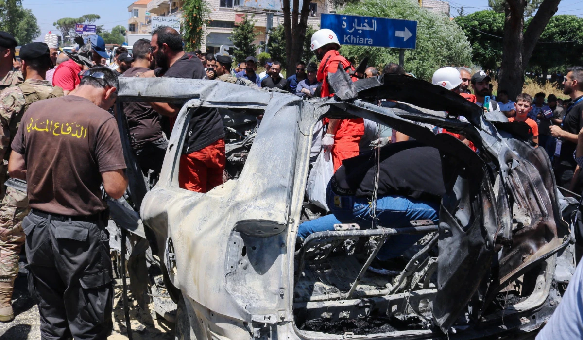 Emergency and security service members and residents gather around the carcass of a car at the site of an Israeli strike in al-Khiyara town in Lebanon's Western Bekaa area on June 22, 2024, which killed a member of the Jamaa Islamiya group according to a Lebanese security source. (AFP)