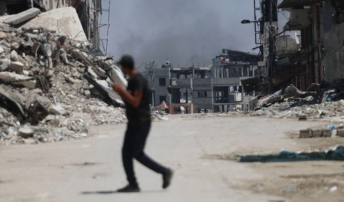 A Palestinian man crosses a street with smoke billowing in the background from an area targeted by Israeli bombardment in the Gaza City district of Shujaiya on June 28, 2024, amid the ongoing conflict between Israel and Hamas. (AFP)