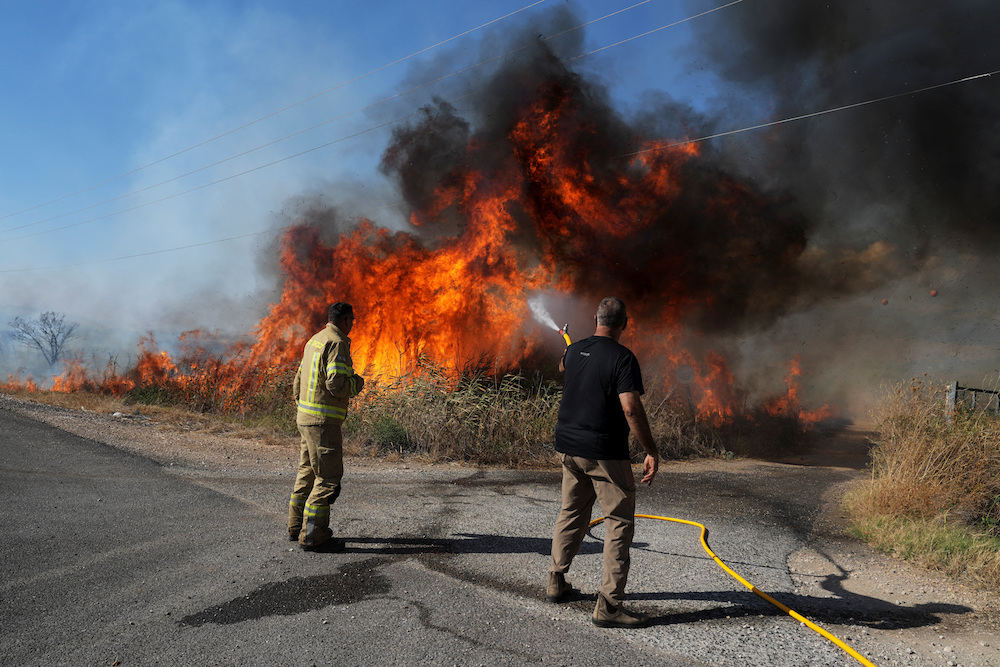 An Israeli firefighter and a man from the immediate responders team work to take control over a fire on the Israeli side of the Israel-Lebanon border amid ongoing cross-border hostilities between Hezbollah and Israeli forces, July 1, 2024. (Reuters)