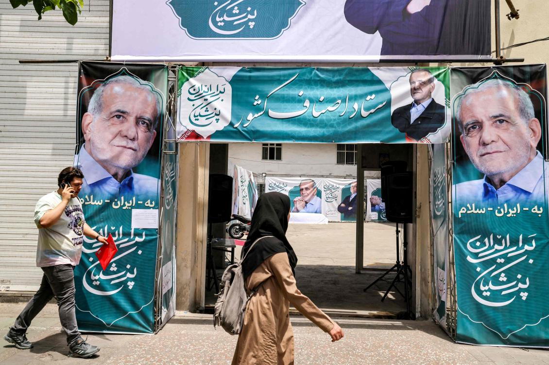 People walk past election banners for Iranian presidential candidate Masoud Pezeshkian along a street in Tehran, on July 2, 2024, ahead of the second round of voting in the presidential elections. (AFP)