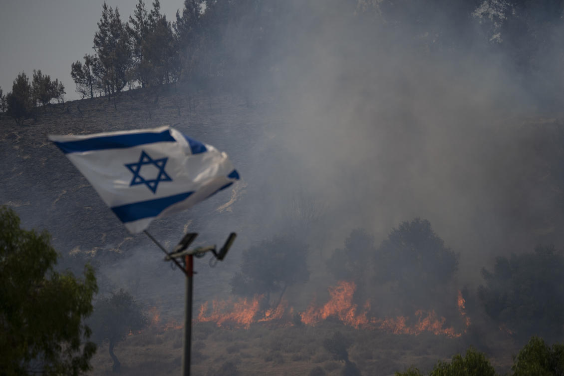 An Israeli flag flutters next to a fire burning in an area near the border with Lebanon, northern Israel in Safed, Wednesday, June 12, 2024. Scores of rockets were fired from Lebanon toward northern Israel on Wednesday morning, hours after Israeli airstrikes killed four officials from the militant Hezbollah group including a senior military commander. (AP)