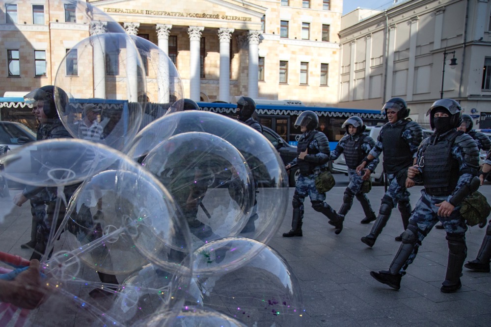 Police officers walk past a balloon seller as they control a street during an unsanctioned rally in front of the Russian General Prosecution building in Moscow. (AP))