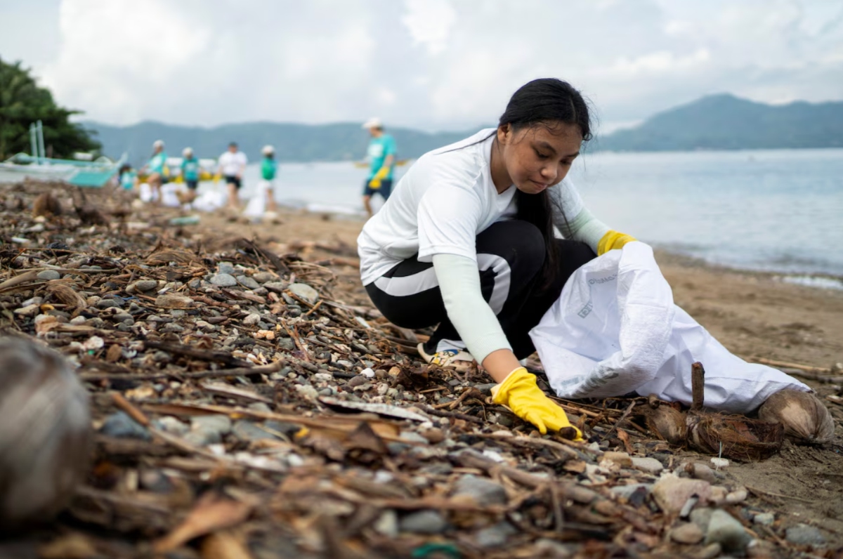A woman collects plastic waste on a beach during a coastal cleanup program which provides rice to volunteers in exchange of plastic waste, in Mabini, Batangas province, Philippines, June 15, 2024. (Reuters)