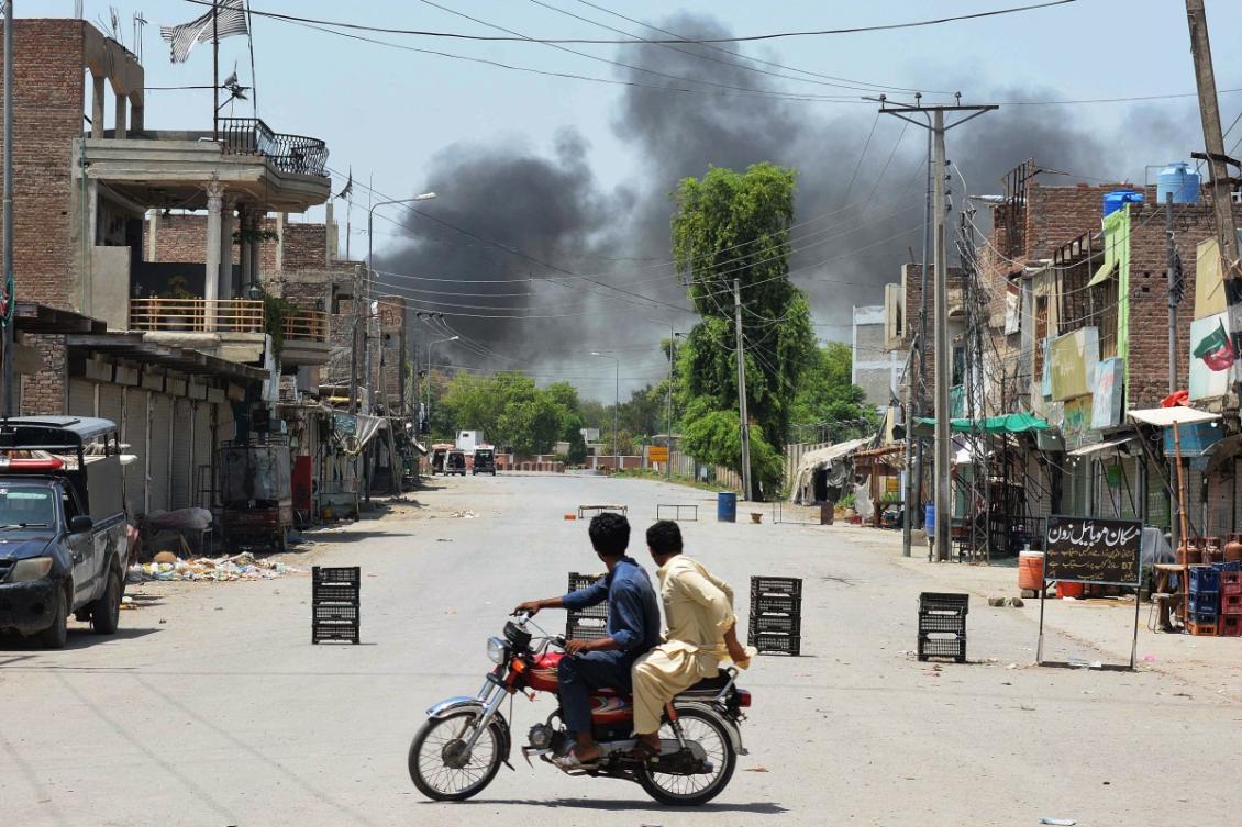 Men riding a bike watch as smoke rises following an explosion allegedly after militants suicide squad attempted to storm an army cantonment that houses military residences and offices in Bannu on July 15, 2024. (AFP)