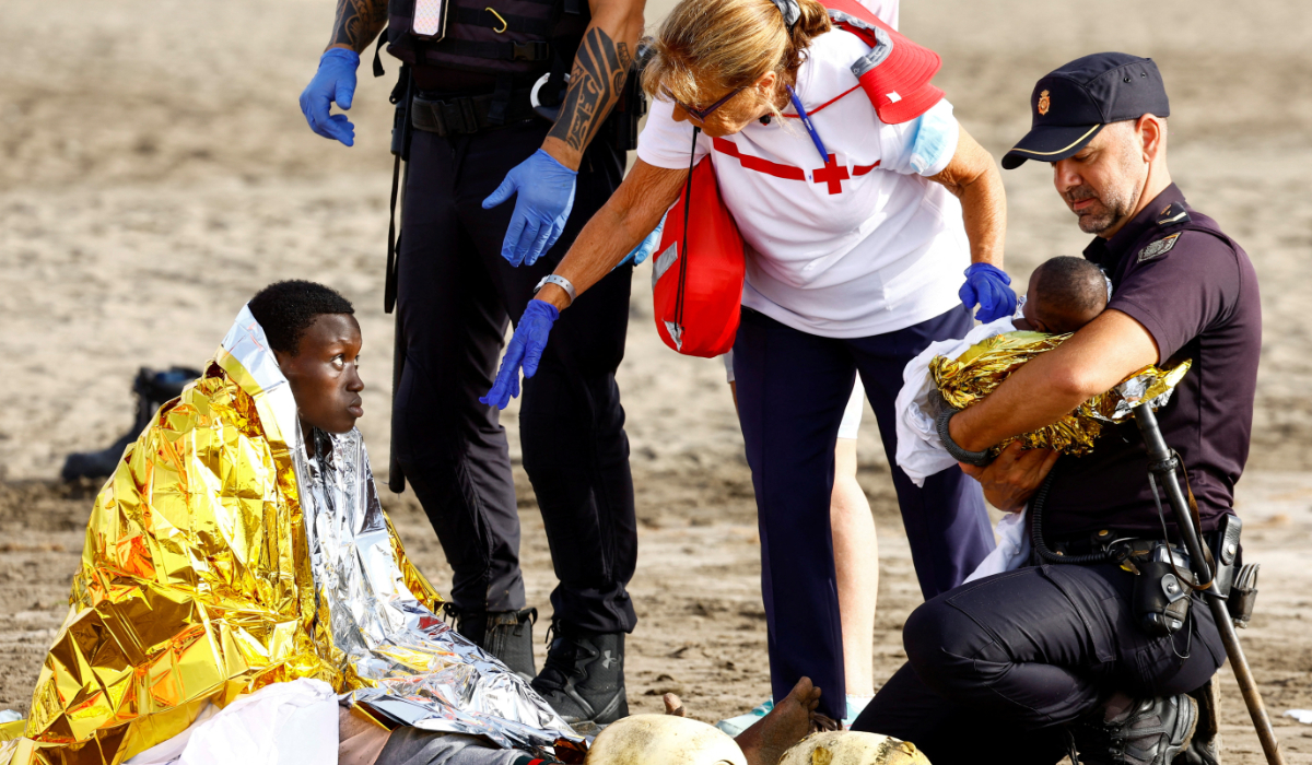 A police officer holds a migrant's baby, while she rests on the sand after arriving in a fiber boat at Las Burras beach in San Agustin, on the island of Gran Canaria, Spain, July 19, 2024. (REUTERS)