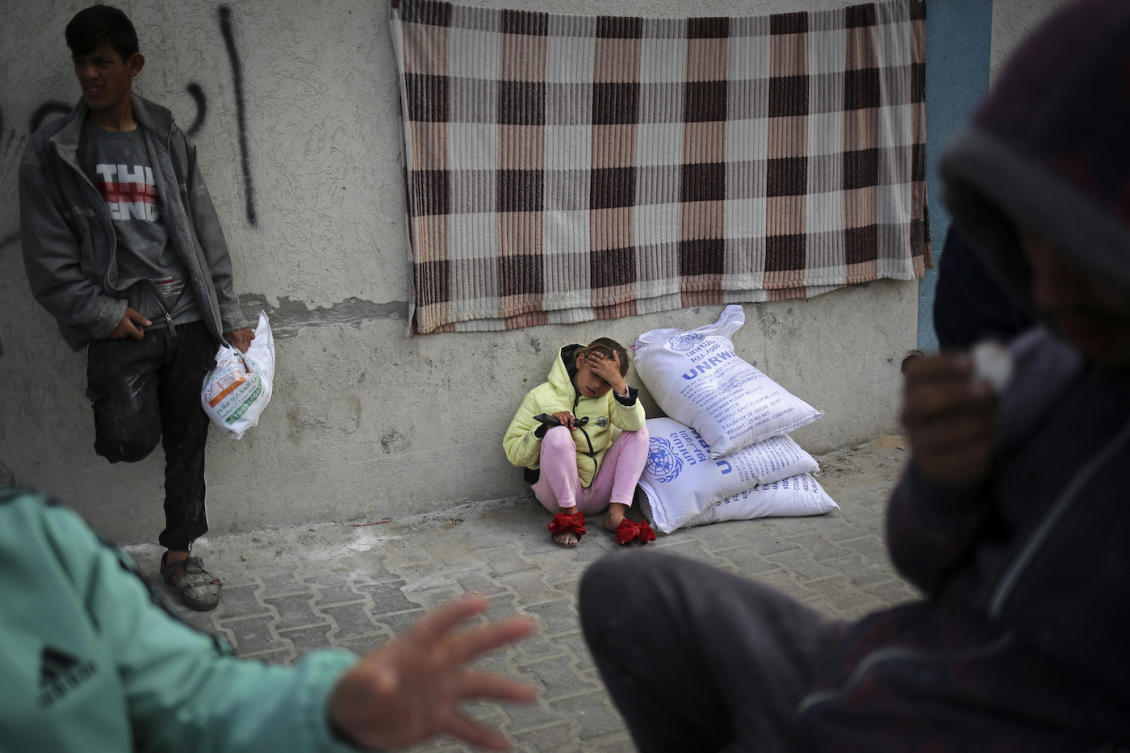 A displaced Palestinian girl sits next to sacks of humanitarian aid at the UNRWA distribution center in Rafah in the southern Gaza Strip. (File/AFP)