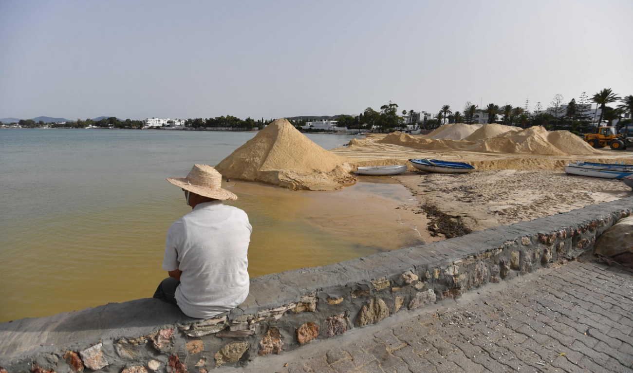 A man looks on as a digger spreads sand on a beach on June 28, 2024, in the tourist town of Hammamet, about 65 KMs southeast of Tunisia’s capital, as authorities fight to protect the coast from rising sea levels and erosion. (AFP)