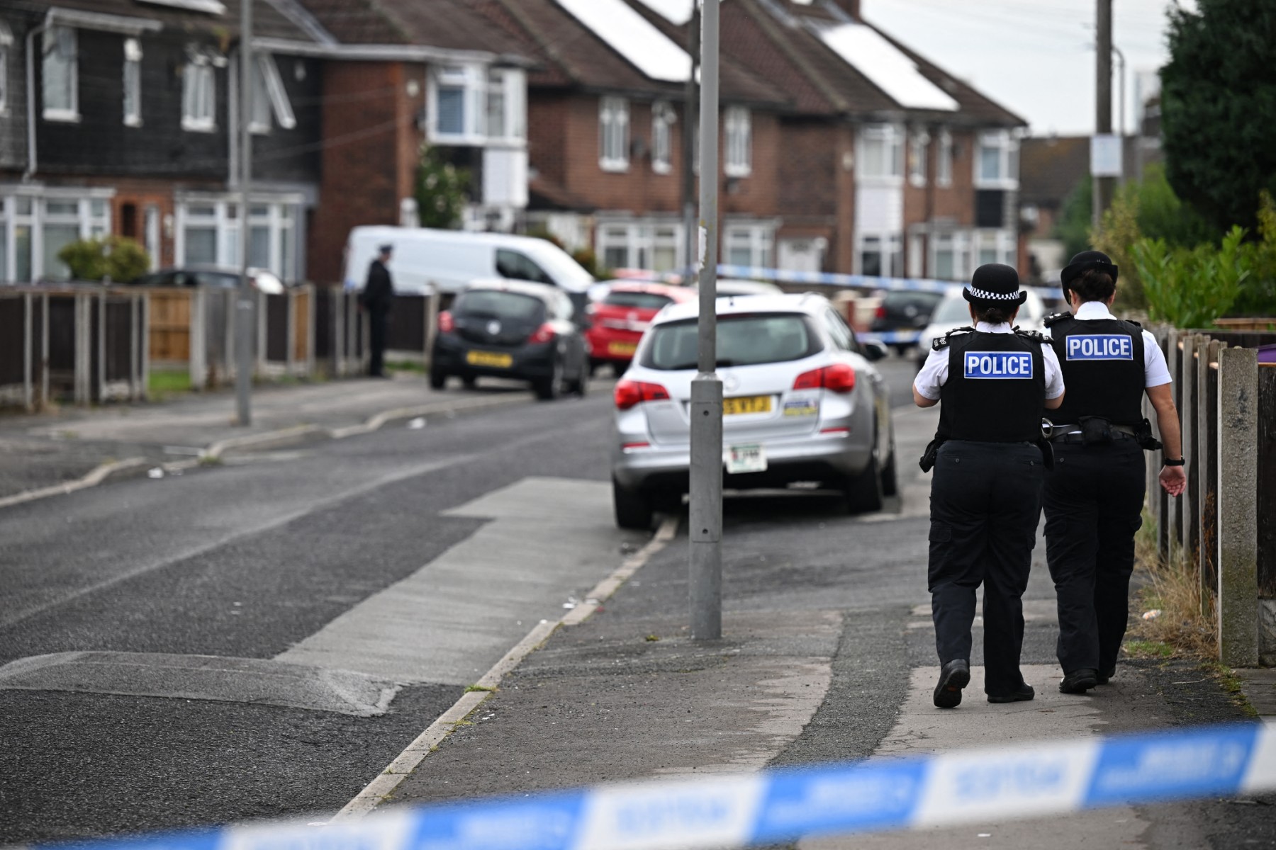 British Police officers walk behind a security cordon by a house in the Knotty Ash area in Liverpool, on August 23, 2022, where a 9 years old girl was shot overnight by a gunman. (AFP)