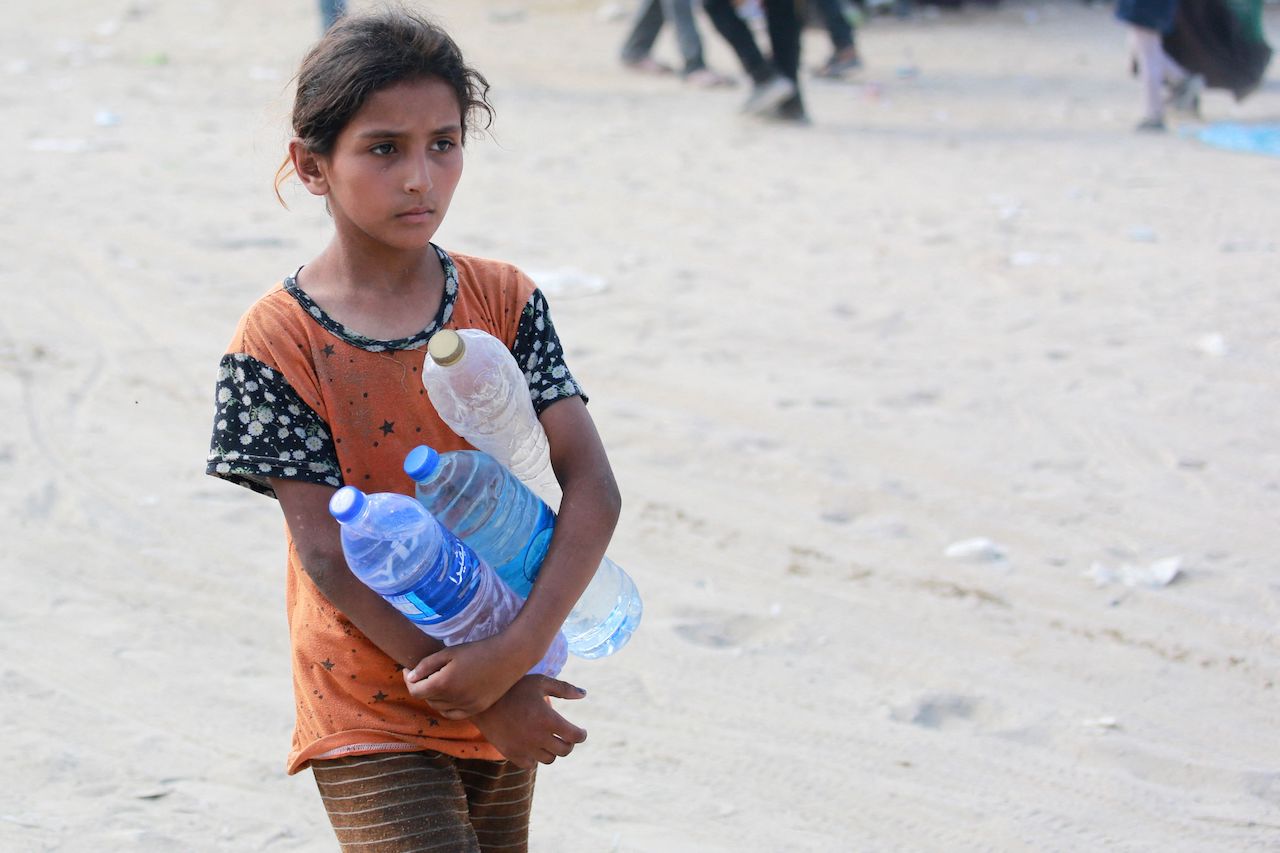 A Palestinian girl caries bottles of water as she walks along a street, as thousands of Palestinians who fled following the Israeli army's temporary evacuation order for parts of Khan Yunis, including the Al-Mawasi humanitarian zone, arrive in an another area of the southern Gaza Strip city on July 23, 2024, as the conflict between Israel and the Palestinian militant group Hamas continues. (AFP)