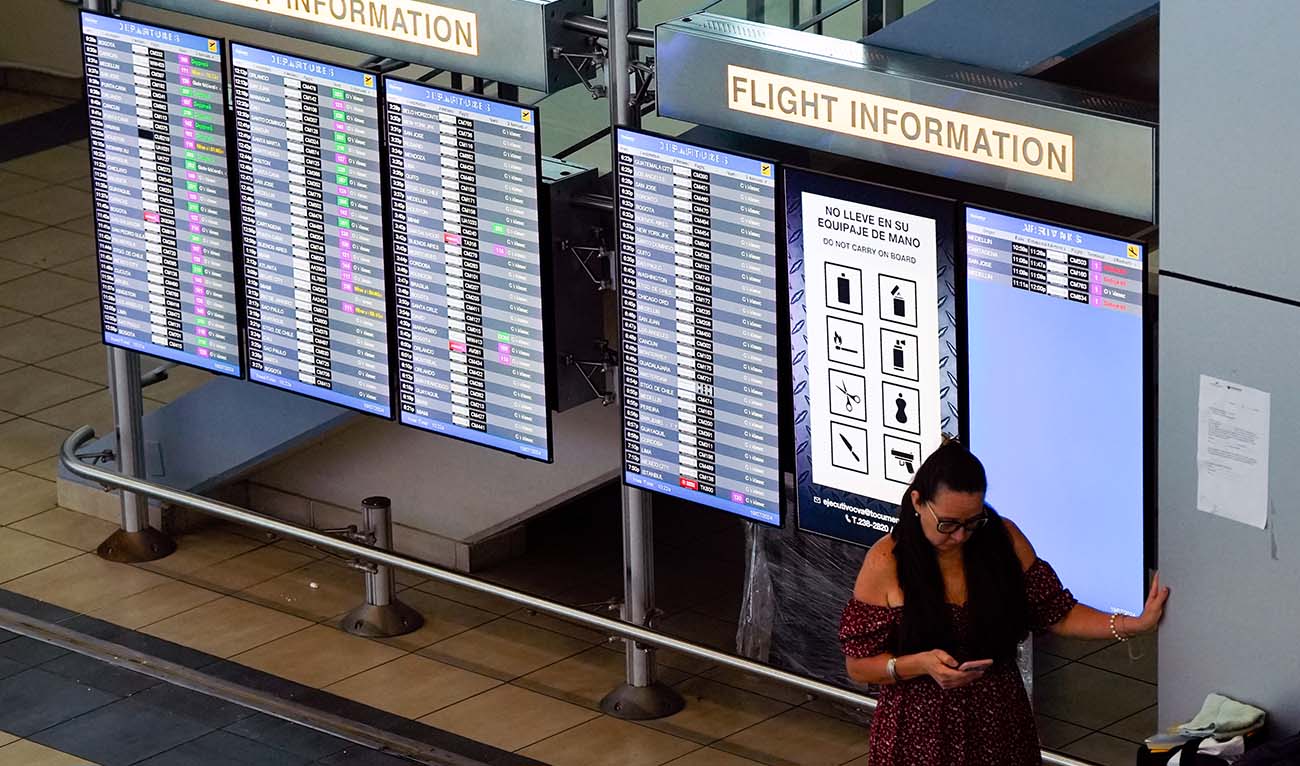 A passenger checks her mobile phone next to monitors display displaying flights information at Tocumen International Airport in Panama City on July 19, 2024, after a bug caused a global outage affecting airports, making it impossible to board planes and forcing multiple delays and cancellations around the world. (AFP/File)
