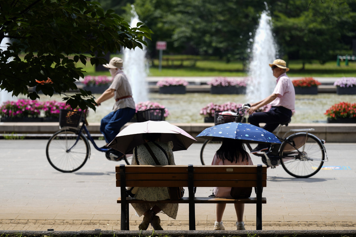 People holding parasols sit on the bench under an intense sun at a park in Tokyo, July 8, 2024. Japan's total population marked the 15th straight year of decline, according to government data released on July 24. (AP)
