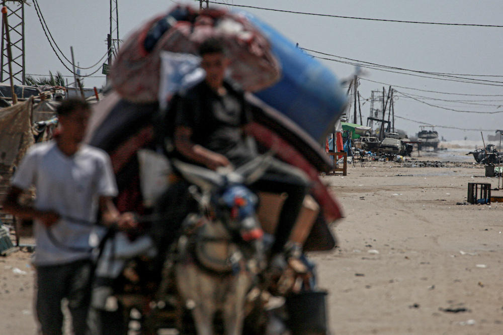 An Israeli tank takes position in the background as displaced Palestinians evacuate from the northwestern outskirts of Rafah in the southern Gaza Strip on June 28, 2024. (AFP file photo)