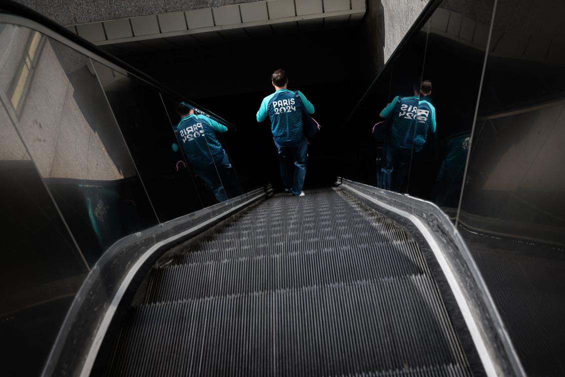 A Paris 2024 Olympic games volunteer walks down an escalator, on July 22, 2024, at the Paris La Defense business district a few days ahead of the Paris 2024 Olympic games opening ceremony. (Photo by Loic VENANCE / AFP)