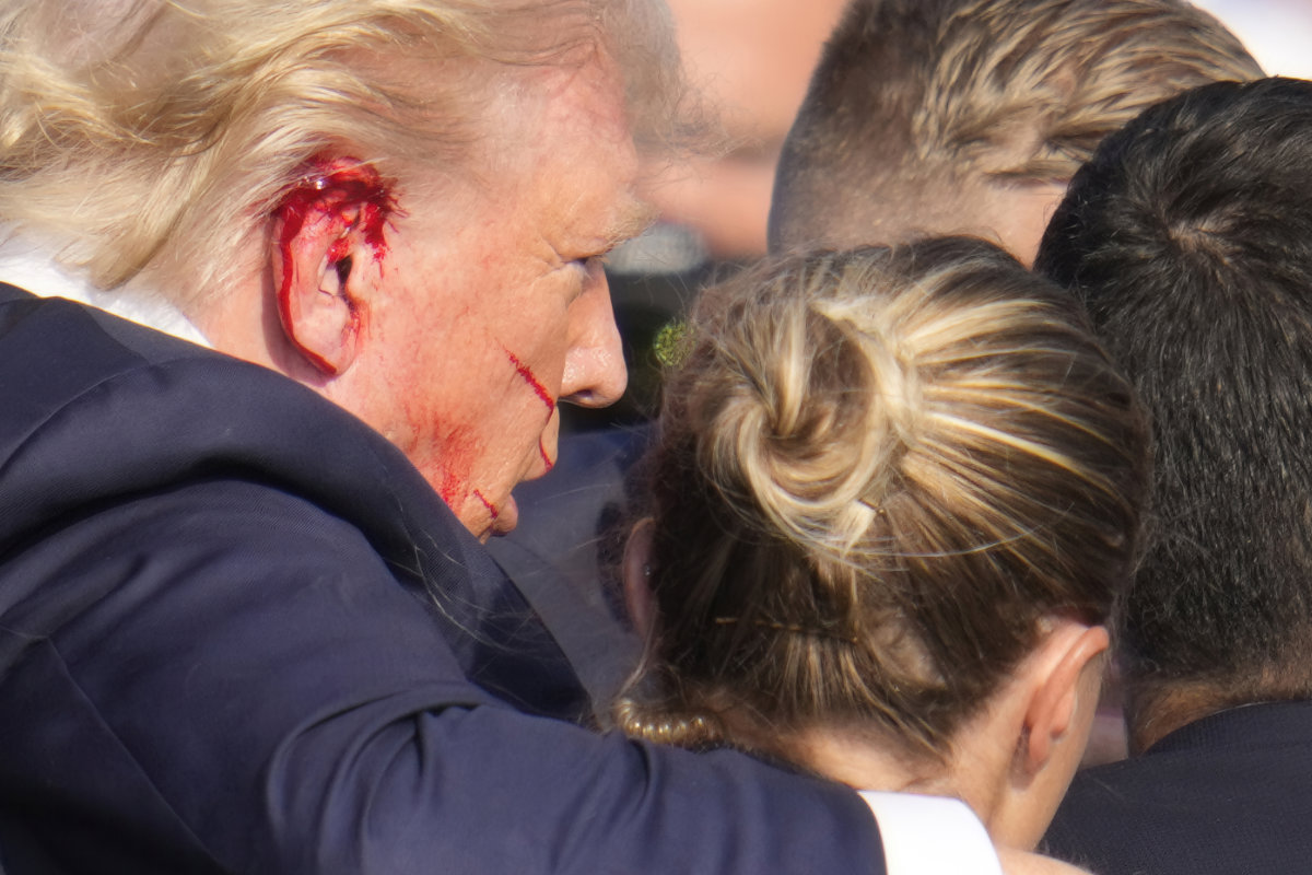 Republican presidential candidate Donald Trump, his ear splattered with blood, is helped off the stage by US Secret Service agents after a 20-year-old assassin fired at him during a campaign rally in Butler, Pennsylvania, on July 13, 2024. (AP Photo/File)