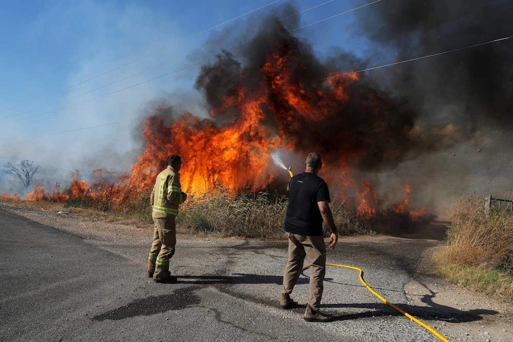 An Israeli firefighter and a man from the immediate responders team work to take control over a fire on the Israeli side of the Israel-Lebanon border amid ongoing cross-border hostilities between Hezbollah and Israeli forces, July 1, 2024. (Reuters)