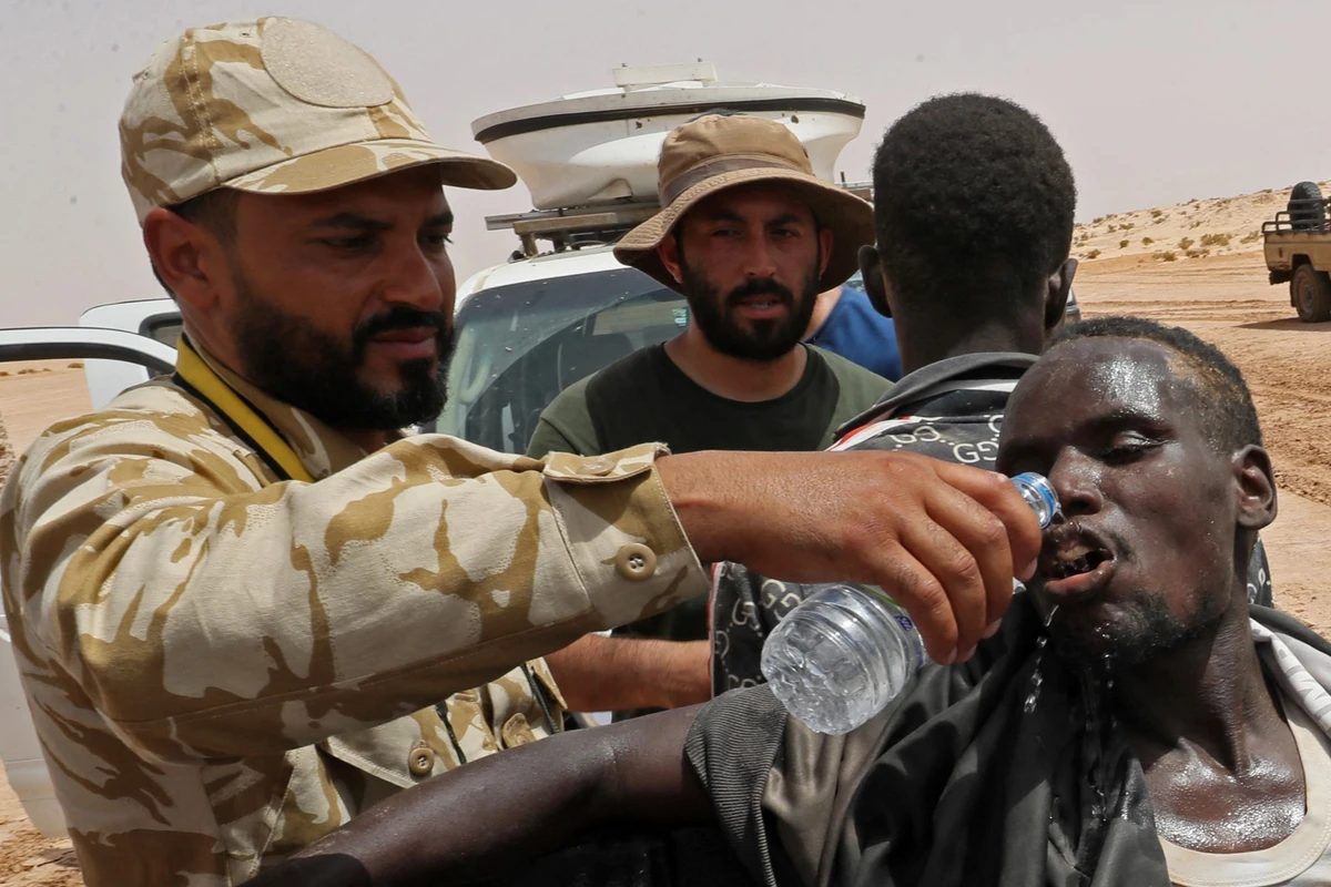 Libyan border guard provide water to migrants of African origin who reportedly have been abandoned by Tunisian authorities, following their arrival in an uninhabited area near Al-Assah on the Libya-Tunisia border on July 30, 2023.(AFP)