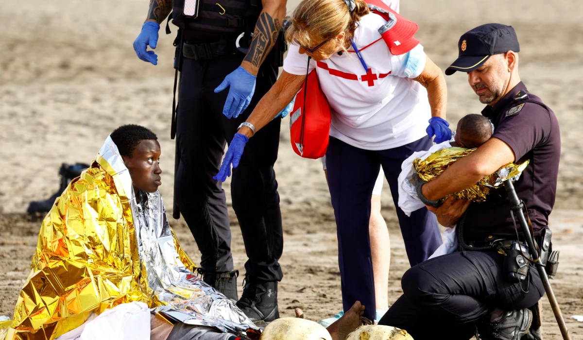 A police officer holds a migrant's baby, while she rests on the sand after arriving in a fiber boat at Las Burras beach in San Agustin, on the island of Gran Canaria, Spain, July 19, 2024. (REUTERS)