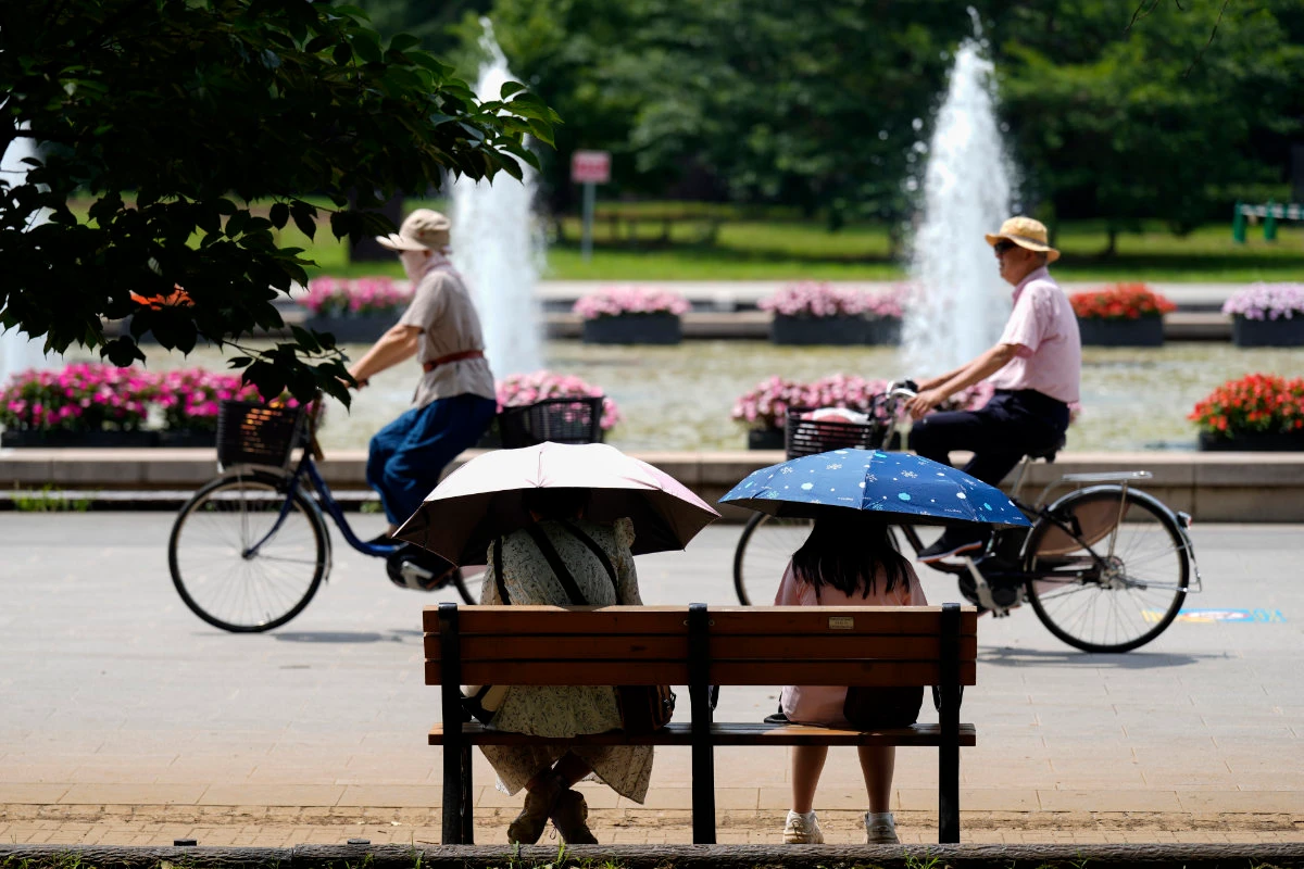 People holding parasols sit on the bench under an intense sun at a park in Tokyo, July 8, 2024. Japan's total population marked the 15th straight year of decline, according to government data released on July 24. (AP)