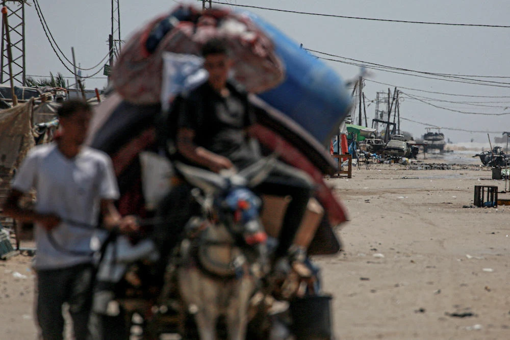 An Israeli tank takes position in the background as displaced Palestinians evacuate from the northwestern outskirts of Rafah in the southern Gaza Strip on June 28, 2024. (AFP file photo)