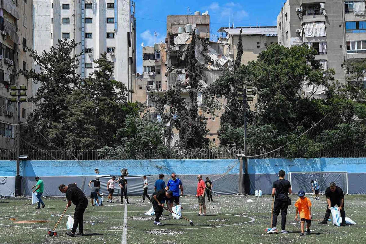Residents clear the rubble in a football field facing the building that was hit a day earlier in an Israeli strike in Beirut’s southern suburbs, on July 31, 2024. (AFP)