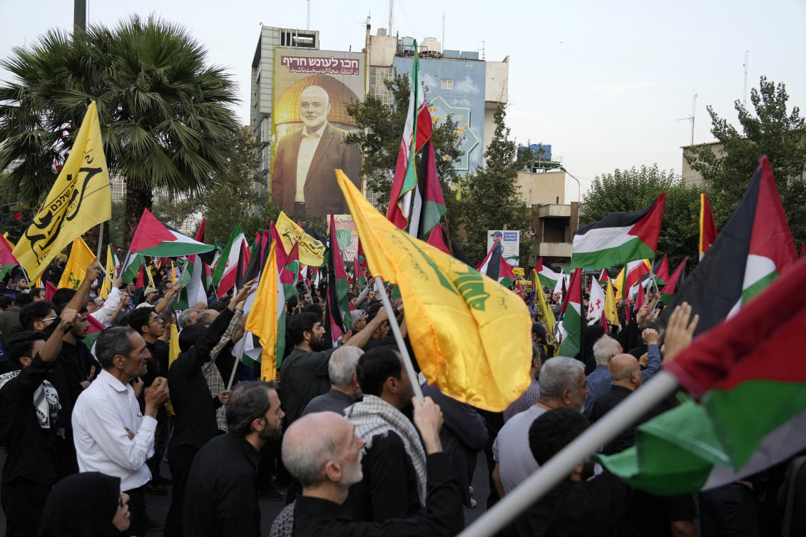 Iranian protesters wave Iranian, Palestinian and Lebanon’s militant Hezbollah group flags in a demonstration to condemn the killing of Hamas leader Ismail Haniyeh as a huge portrait of him is seen on a wall at background, at Felestin (Palestine) Sq. in Tehran (AP)