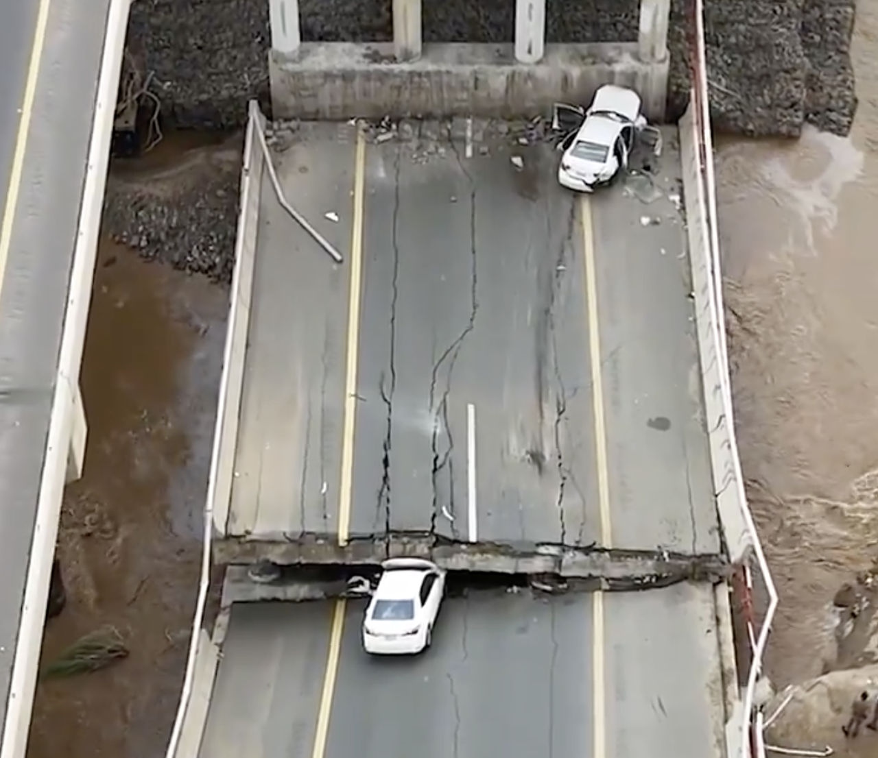 Al-Ekhbariya aired images of two vehicles caught up in the floodwaters, one of them crushed by a collapsed bridge support. (Screenshot)