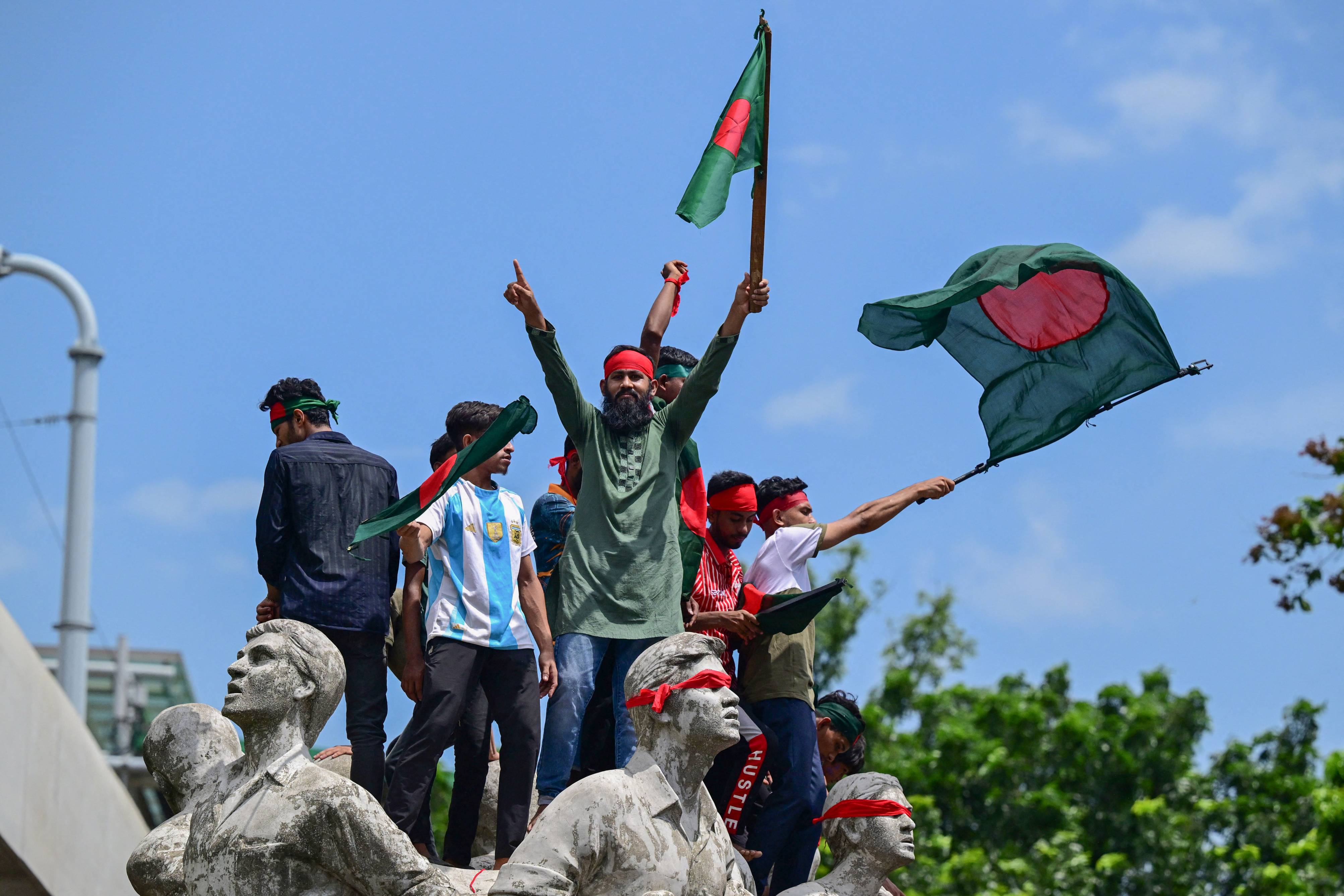 Protesters wave national flags as they stand over the Anti Terrorism Raju Memorial Sculpture during a protest in Dhaka on Aug. 4, 2024. (AFP)