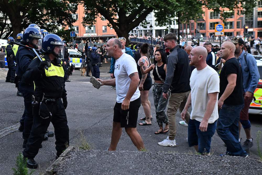 A protester holding a piece of concrete walks towards riot police as clashes erupt in Bristol on Aug. 3, 2024 during a demonstration held in reaction to the fatal stabbings in Southport on July 29. (AFP)