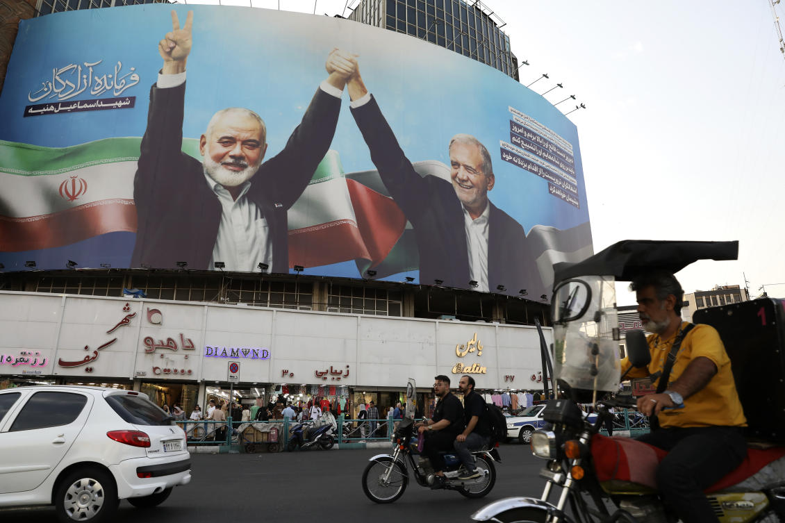 Vehicles drive past a huge banner showing the late Hamas leader Ismail Haniyeh, left, who was killed in an assassination last week, joining hands with Iranian President Masoud Pezeshkian, in a square in downtown Tehran on Aug. 5, 2024. (AP)