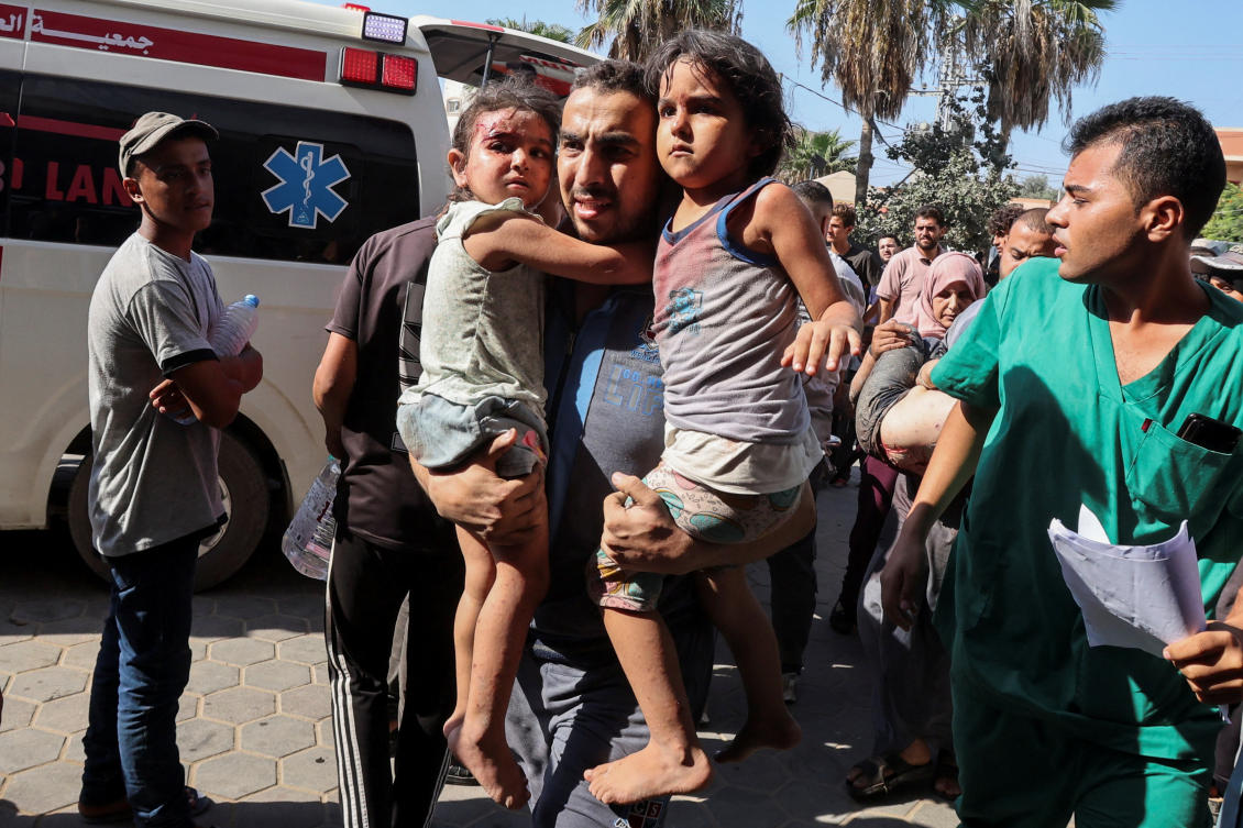 A Palestinian man carries children wounded in an Israeli strike at Al-Aqsa Martyrs Hospital in Deir Al-Balah in the central Gaza Strip, August 18, 2024. (Reuters)