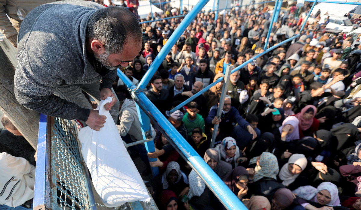 A Palestinian man holds a flour bag as others wait to receive theirs from the United Nations Relief and Works Agency (UNRWA) during a temporary truce between Hamas and Israel, in Khan Younis in the southern Gaza Strip, November 29, 2023. (REUTERS)