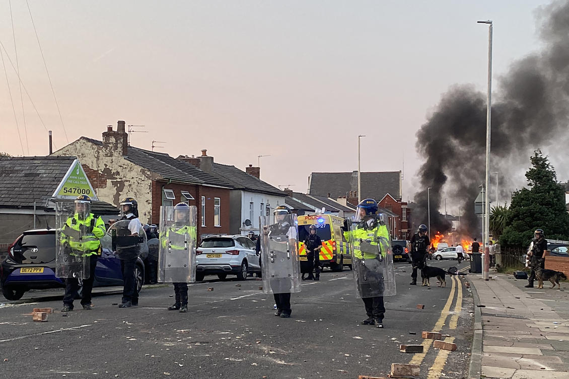 Smoke billows from a fire started by protesters as riot police stand guard after disturbances near the Southport Islamic Society Mosque in northwest England. (File/AFP)