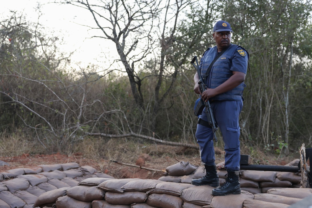 A armed South African Police Services (SAPS) officer stands near the entrance to a farm where they detained ninety five Libyan nationals for receiving training at what authorities suspect to be a secret military camp in White River, Mpumalanga province on July 27, 2024.(AFP)