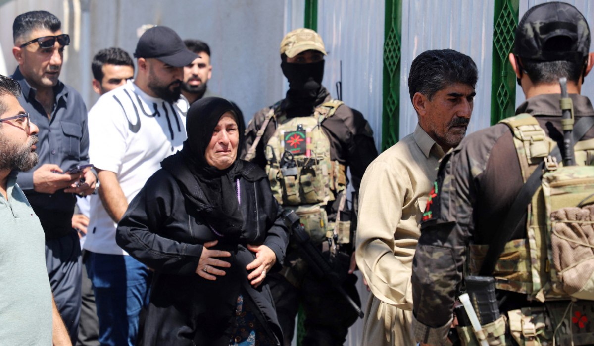The mother (C) and father (2-R) of one of two women journalists killed in a drone strike walk past Kurdish Asayish security forces as relatives and journalists gather in front of the forensic department where the bodies of the two women were brought, in Sulaimaniyah in Iraq's autonomous Kurdistan region on August 23, 2024. (AFP)