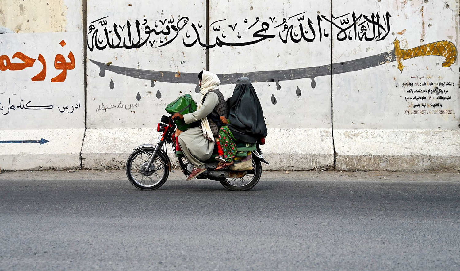 An Afghan man and a burqa-clad woman ride a motorcycle along a street on the outskirts of Kandahar on August 24, 2024. (AFP)