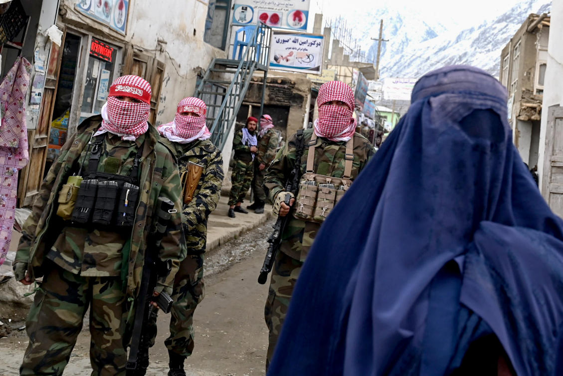 Taliban security personnel stand guard as an Afghan burqa-clad woman walks along a street at a market in the Baharak district of Badakhshan province. (File/AFP)