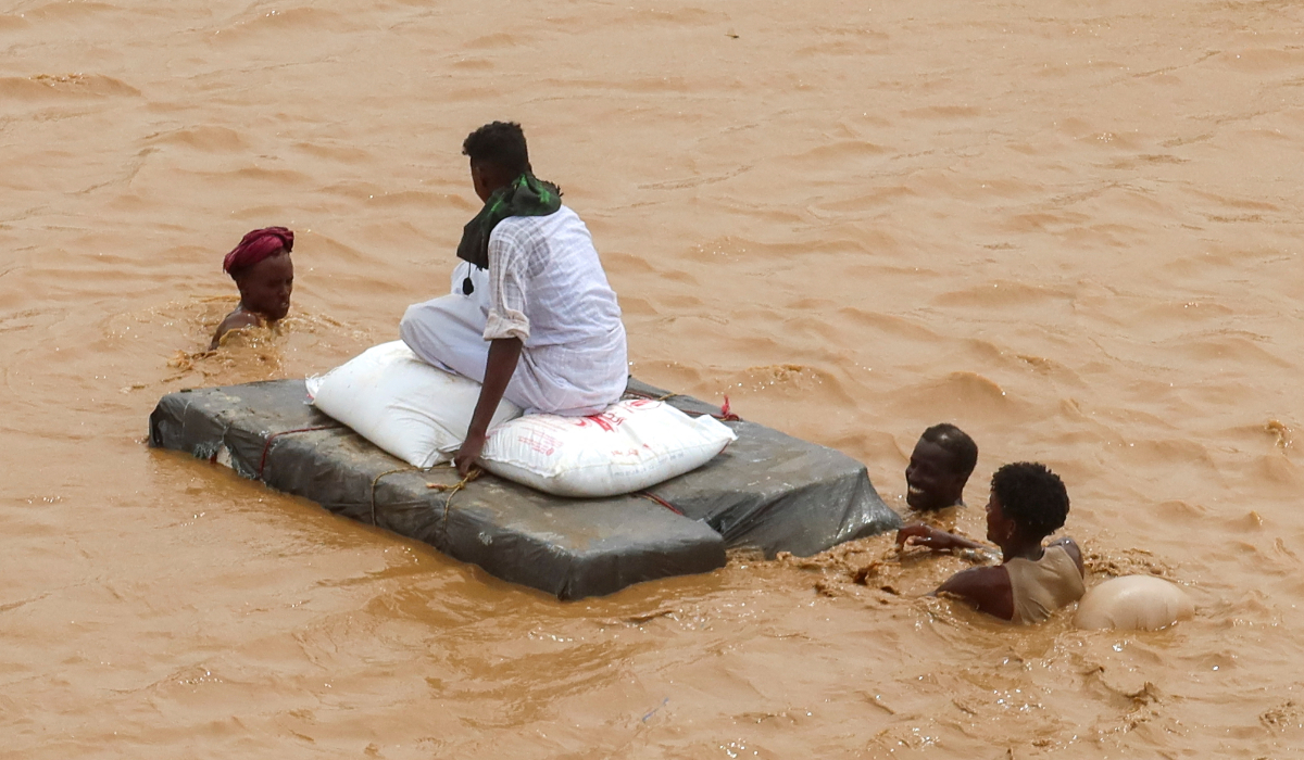 A person sits on bags of aid on a makeshift raft while others wade through flood water, following devastating floods, in South Tokar, Red Sea State, Sudan, August 28, 2024. (REUTERS)