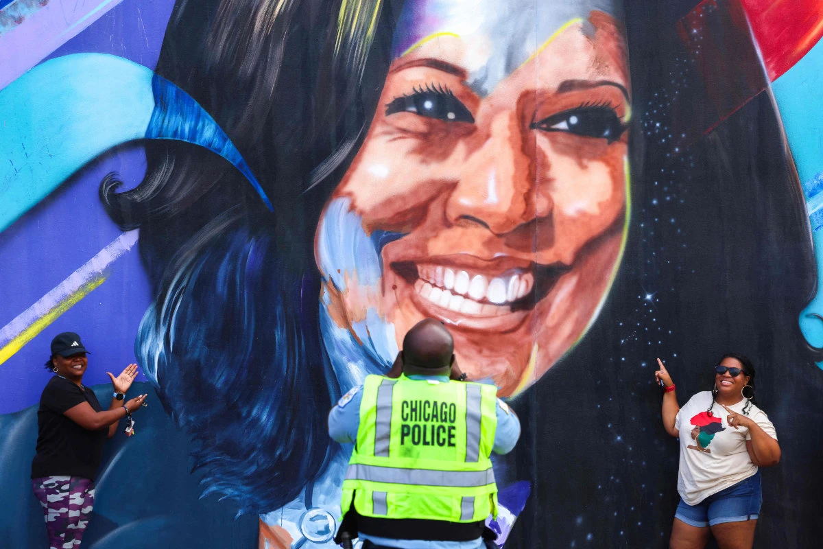 A Chicago police officer takes a picture of people posing before a mural of Democratic presidential nominee US Vice President Kamala Harris outside the United Center ahead of the Democratic National Convention (DNC) in Chicago, Illinois on August 17, 2024. (AFP)