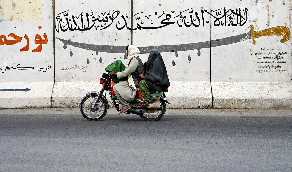 An Afghan man and a burqa-clad woman ride a motorcycle along a street on the outskirts of Kandahar on August 24, 2024. (AFP)