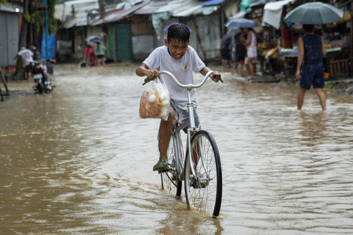 A boy carrying a plastic bag with bread and eggs, rides his bike through a flooded road after heavy rains brought by Tropical storm Yagi, locally known as Enteng, in Baras, Rizal province, Philippines. (Reuters)