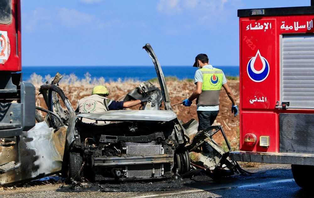 Civil Defense teams inspect a charred car that was hit by an Israeli drone strike on the road leading to the southern Lebanese coastal town of Naqoura, on the border with Israel, Sept. 2, 2024. (AFP)