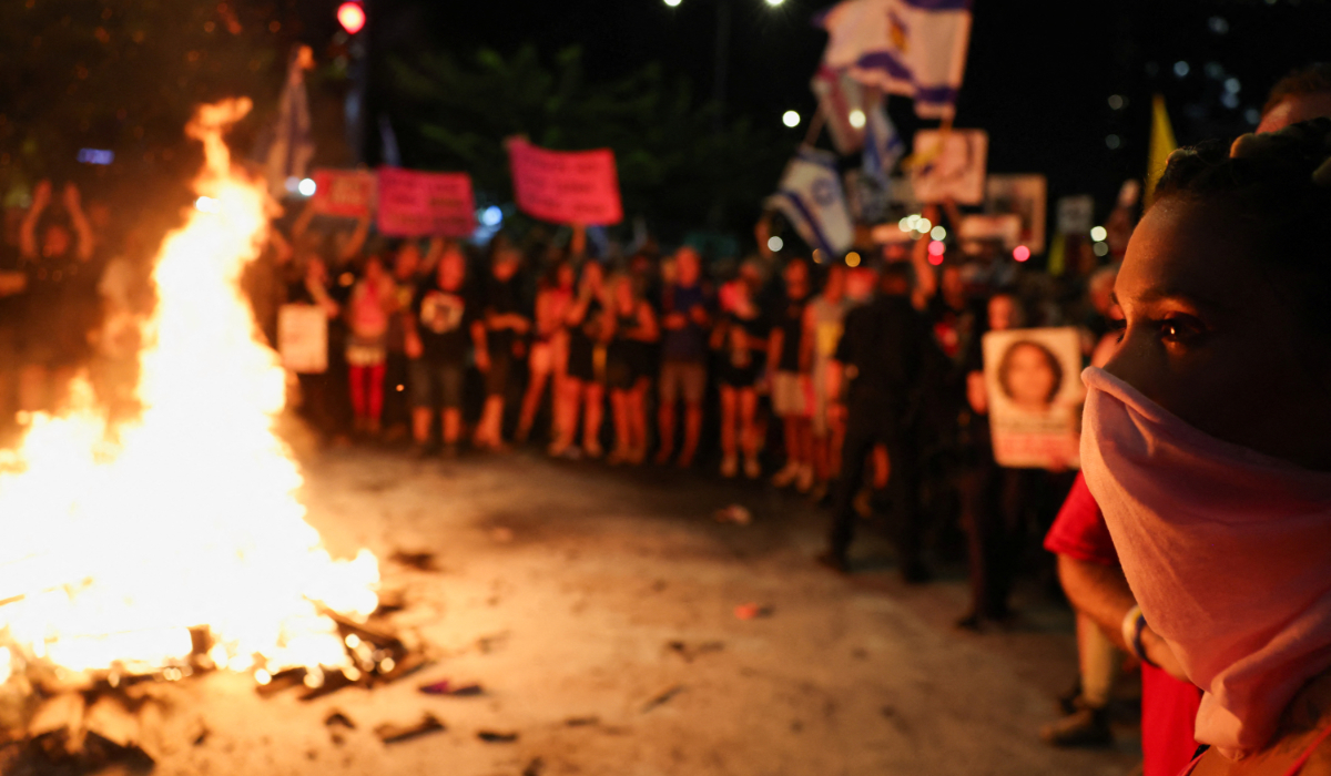 A woman looks on while demonstrators gather around a fire during a demonstration against Israeli Prime Minister Benjamin Netanyahu's government and to call for the release of hostages in Gaza, amid the Israel-Hamas conflict, in Tel Aviv, Israel, September 7, 2024. (REUTERS)