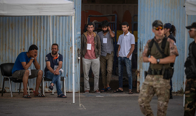 In this photograph, taken on June 15, 2023, survivors of a shipwreck stand at a warehouse at the port in Kalamata town, after a boat carrying dozens of migrants sank in international waters in the Ionian Sea. (AFP/File)