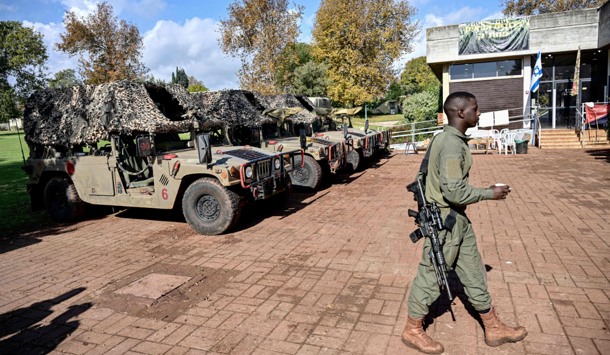 An Israeli army soldier walks with a cup and a cigarette past parked humvees on January 4, 2024 in the evacuated Kibbutz Dafna in northern Israel, about a kilometre away from the border with Lebanon. (AFP)