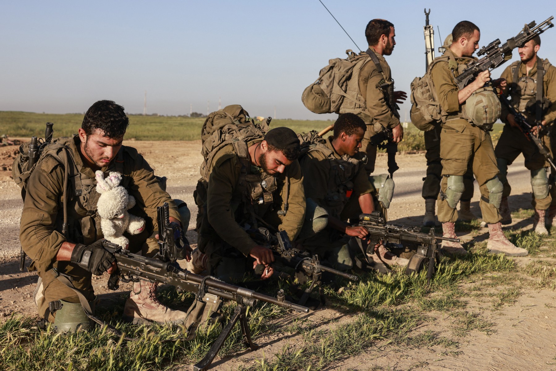 n Israeli soldier carrying a stuffed animal unloads his weapon along other soldiers after coming out from the Gaza Strip, (AFP)