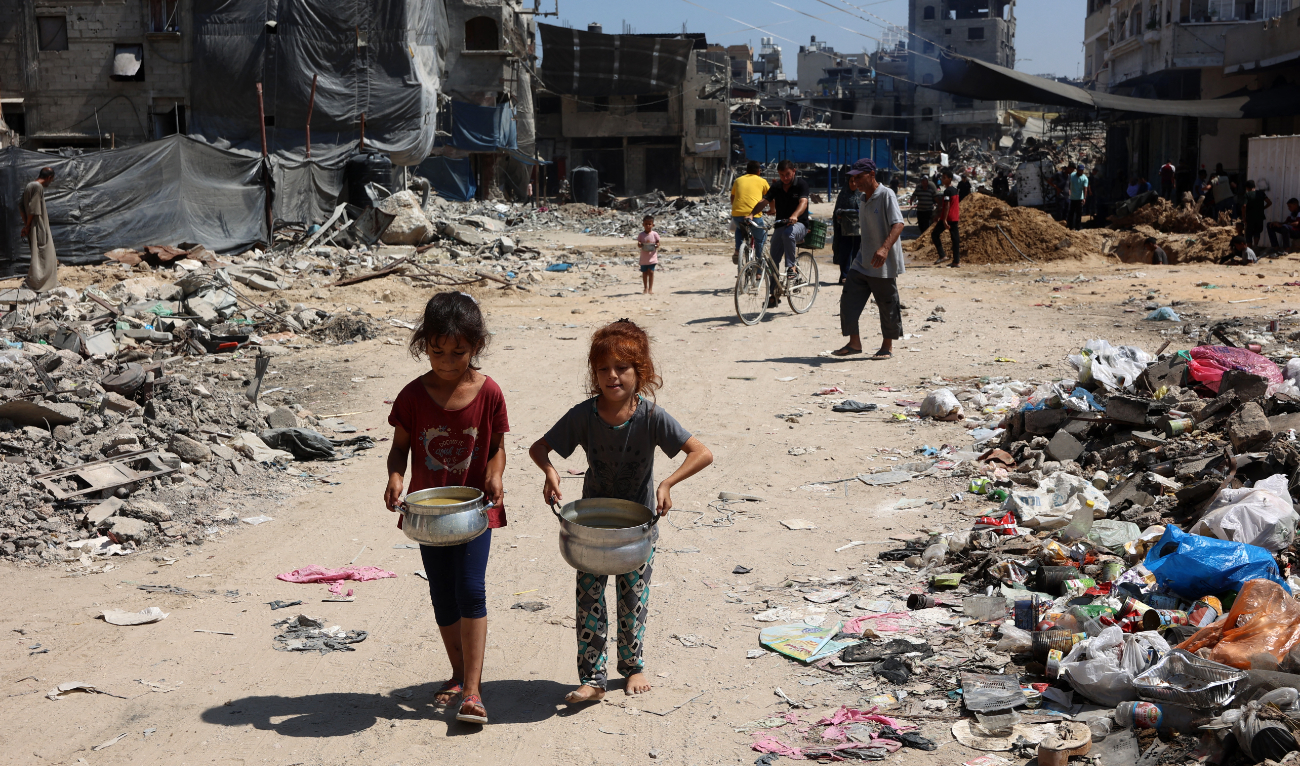 Palestinian children carry pots of soup near a food distribution point in the Jabalia refugee camp in northern Gaza Strip on August 21, 2024. (AFP/File)